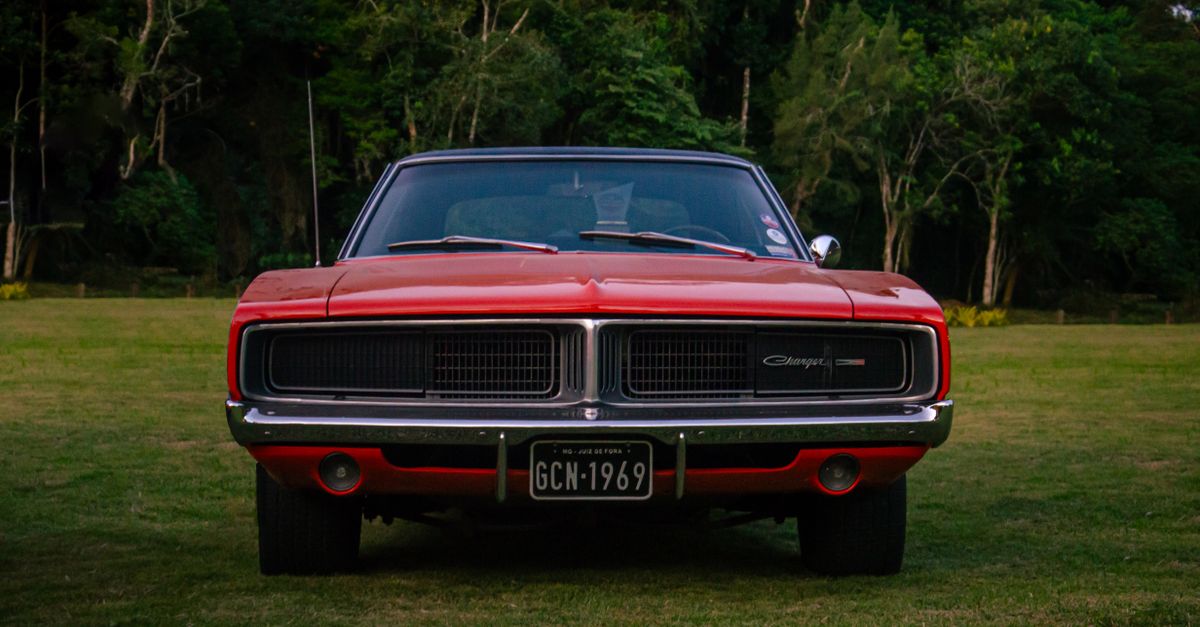 Front view of a classic red Dodge Charger parked in a lush outdoor setting, showcasing retro charm.