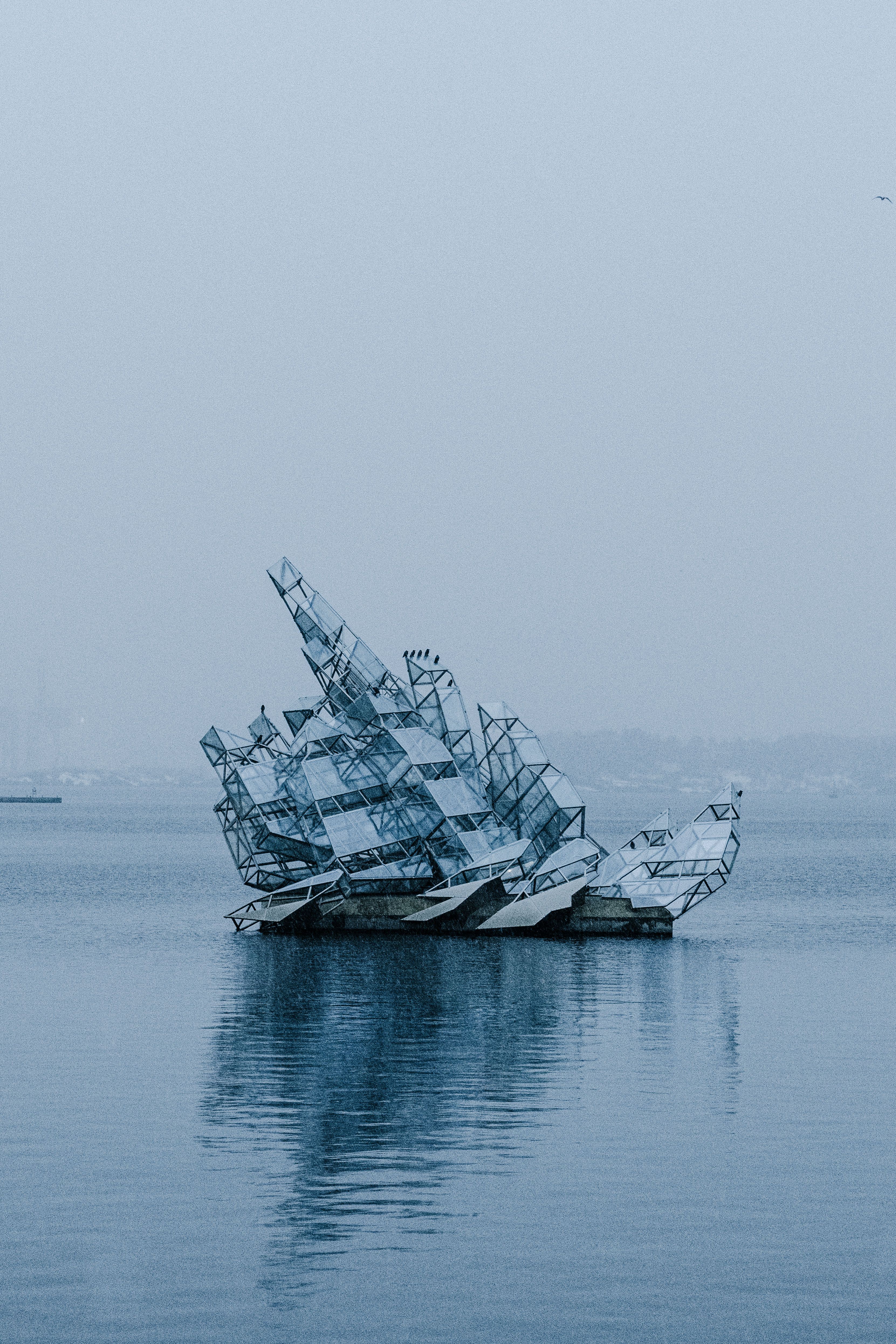 Sculpture resembling a fragmented boat floating on the Oslo Fjord in a serene, misty setting.