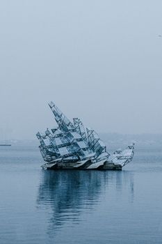 Sculpture resembling a fragmented boat floating on the Oslo Fjord in a serene, misty setting.