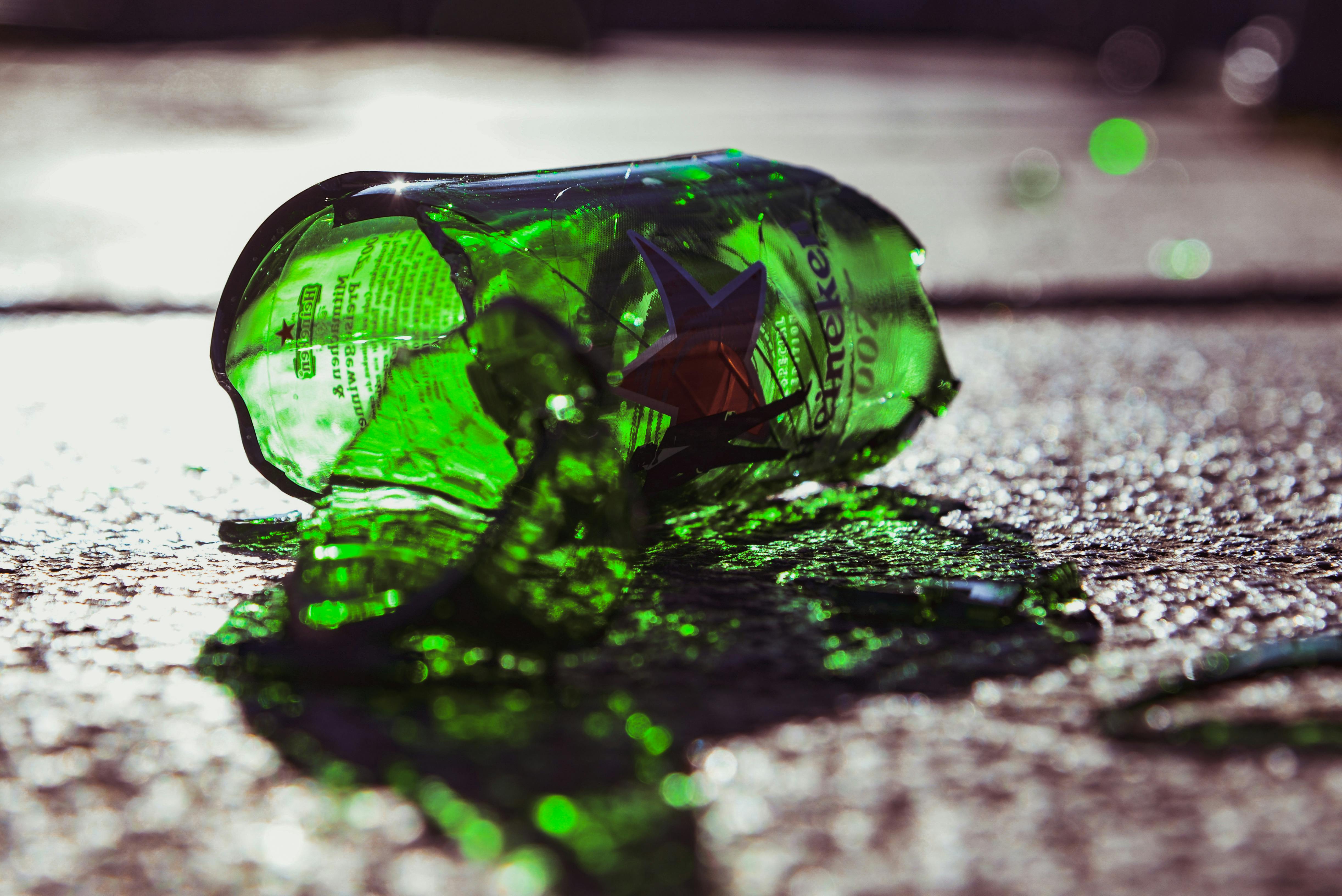 Close-up of a shattered green glass bottle on sunlit pavement, symbolizing litter.