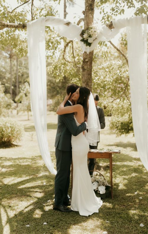 Free Bride and groom embrace under an archway during a beautiful outdoor wedding ceremony. Stock Photo