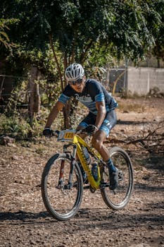 Cyclist riding through rugged terrain in a mountain biking competition under a sunny sky.