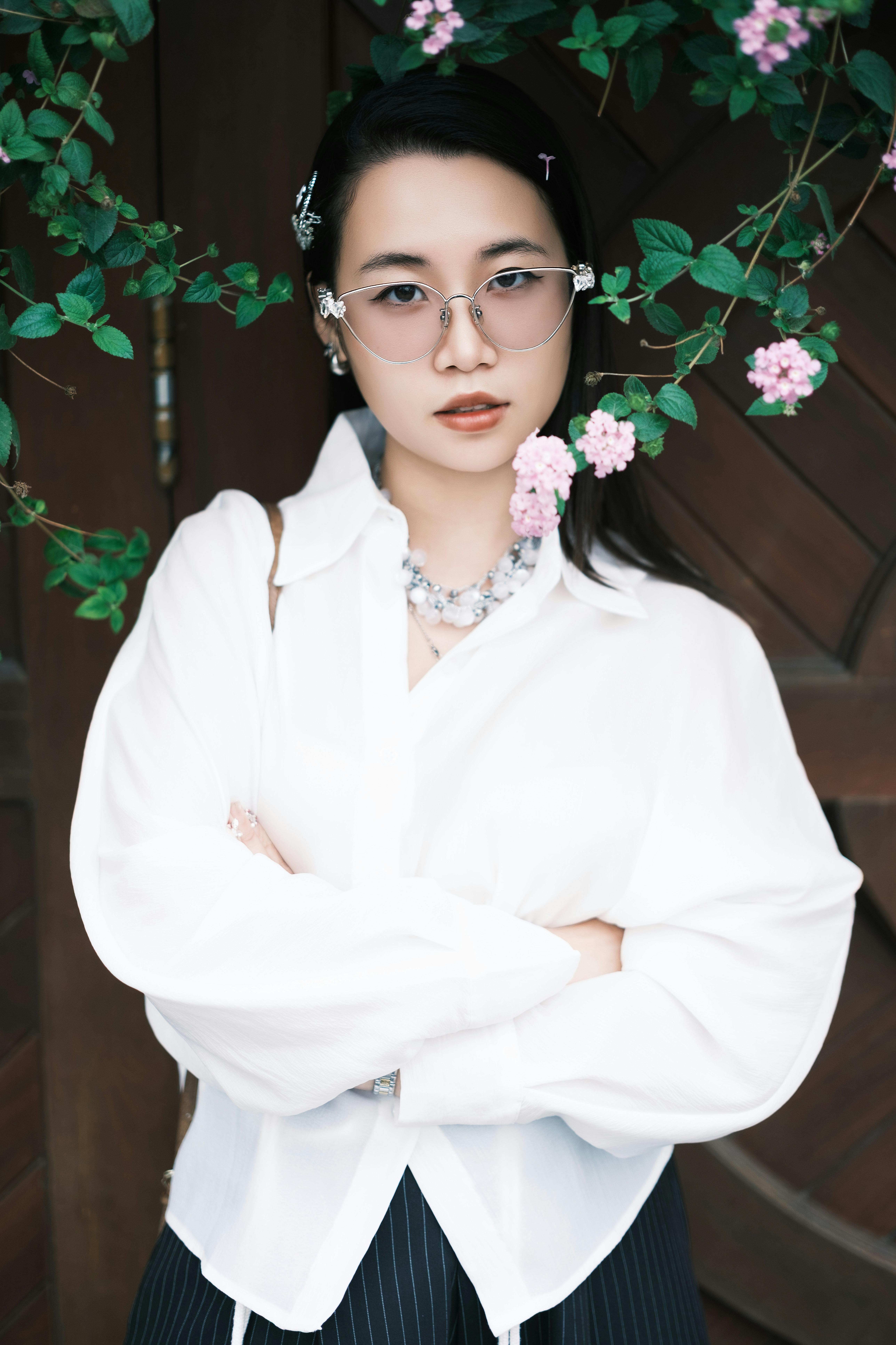 Elegant woman poses confidently surrounded by pink flowers, exuding style and grace.
