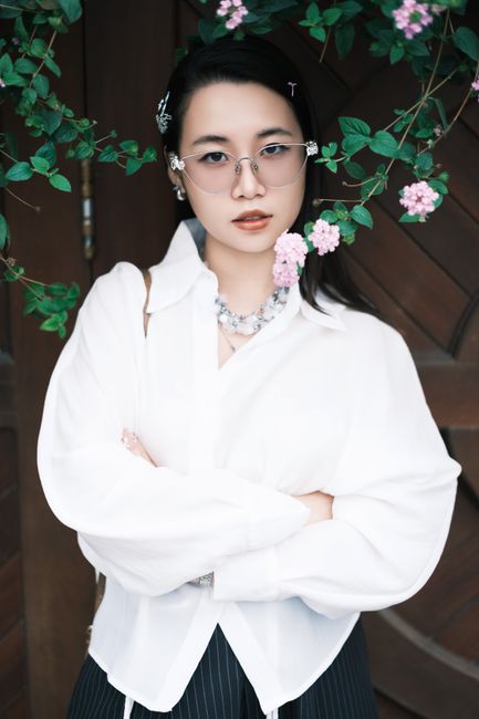 Elegant woman poses confidently surrounded by pink flowers, exuding style and grace.
