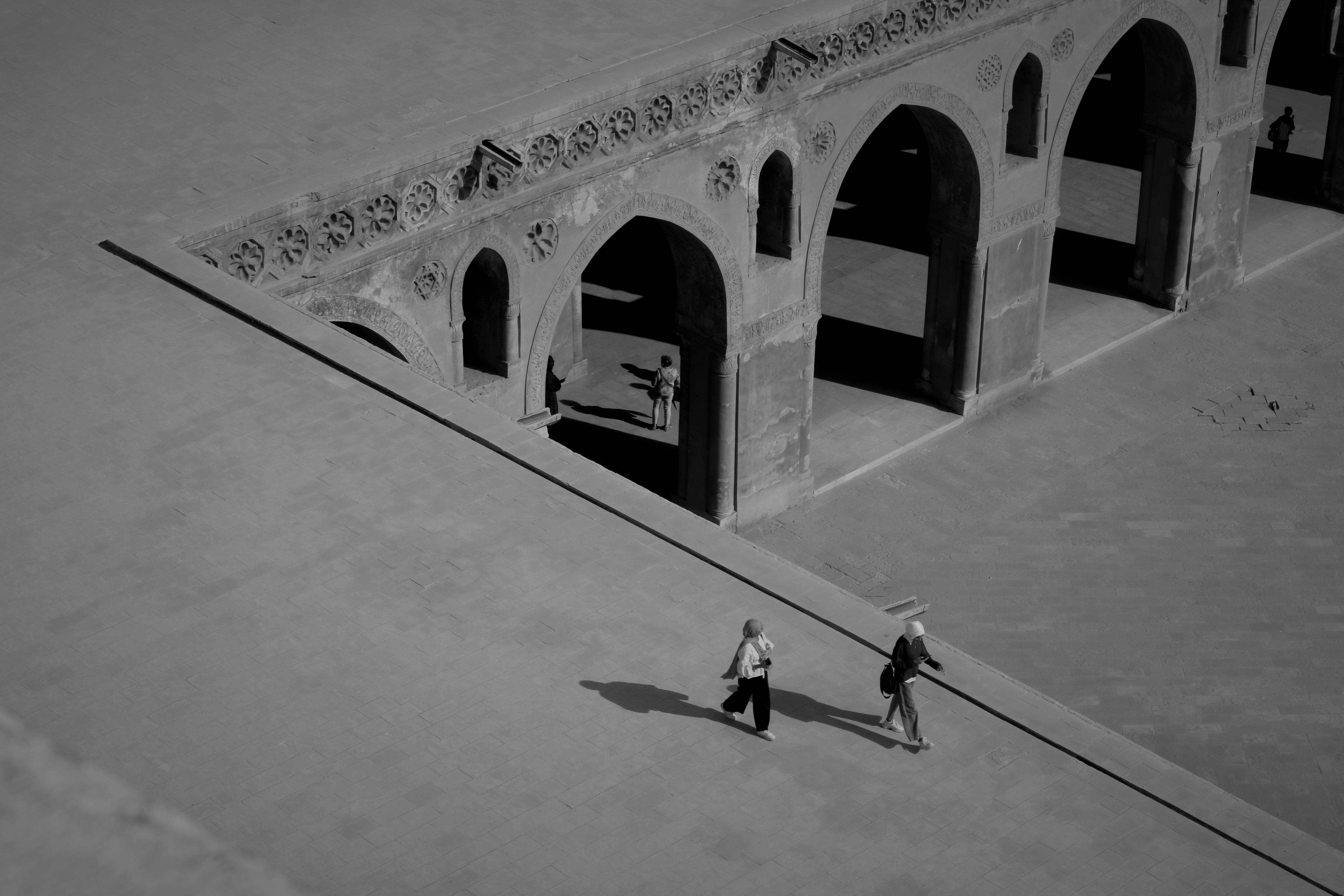 Ücretsiz Bir avludaki tarihi kemerlerin önünden geçen insanları gösteren siyah beyaz bir hava fotoğrafı. Stok Fotoğraflar