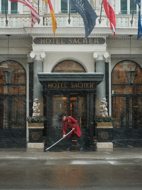 A doorman in red uniform sweeps snow in front of the historic Hotel Sacher in Vienna, Austria.