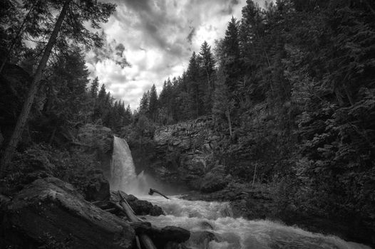 A tranquil waterfall surrounded by dense forest under dramatic clouds.