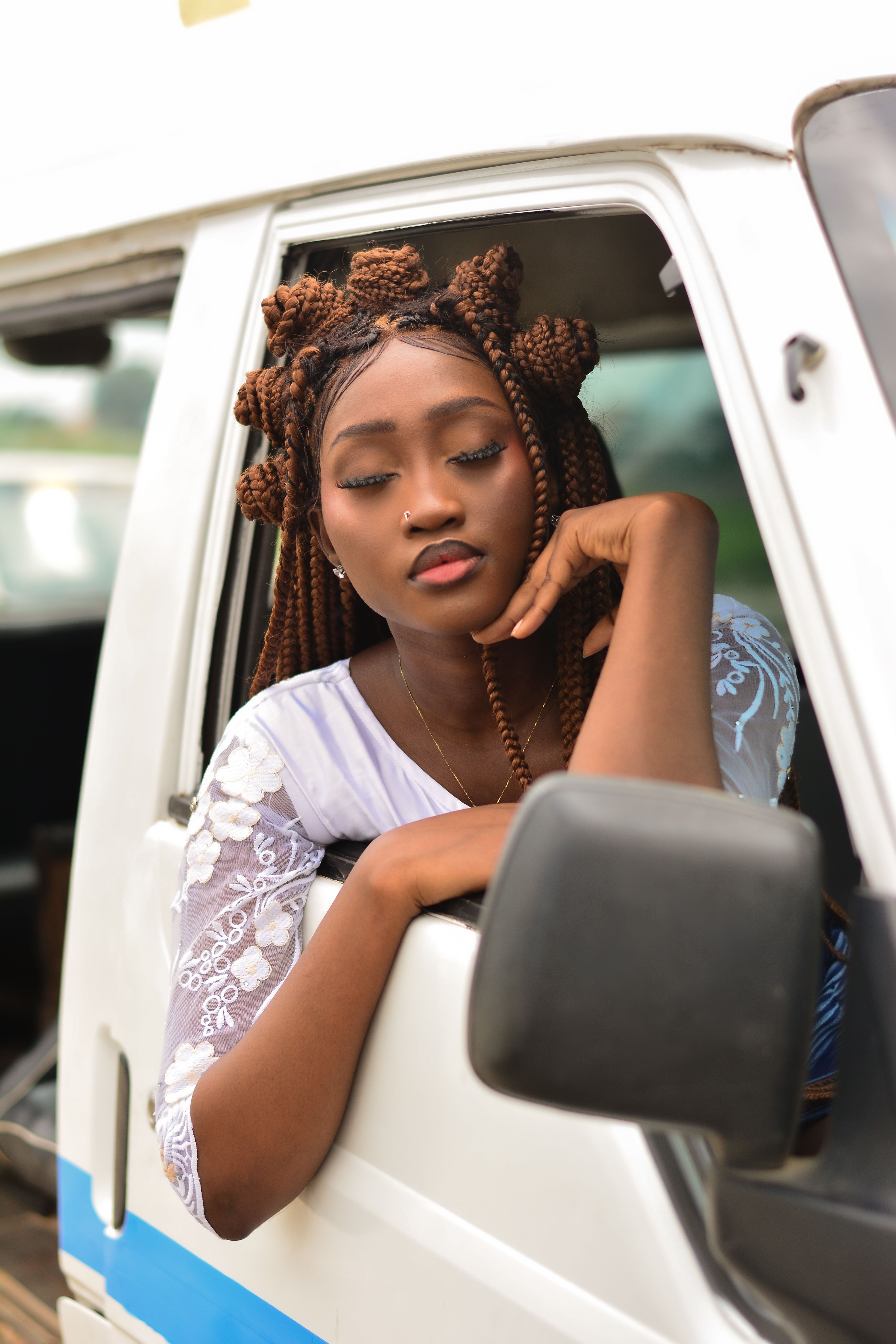 Young woman with braided hair relaxing by the window of a car, conveying a sense of calm and contemplation.