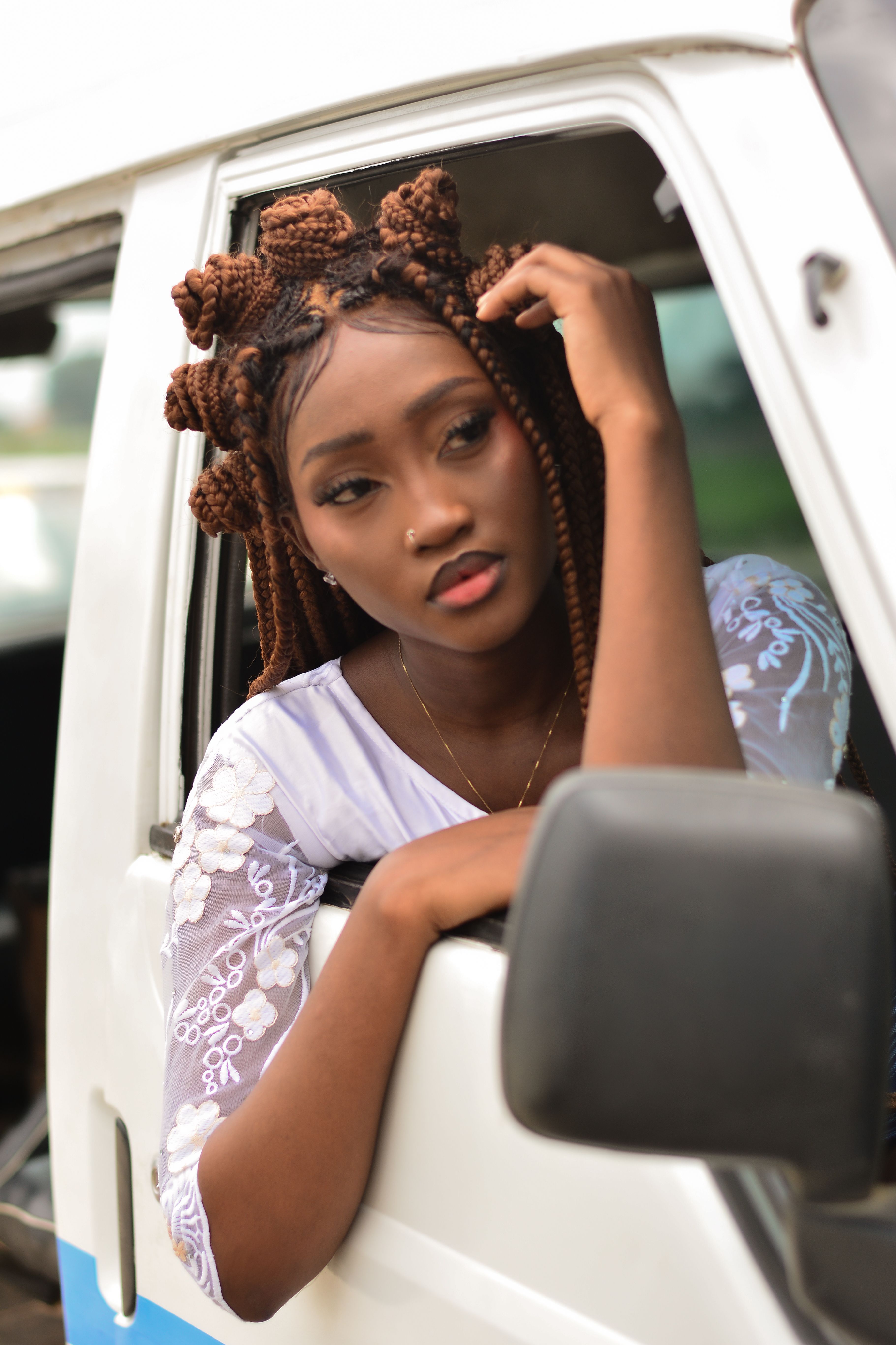 Portrait of a young woman with braided hair gazing out of a vehicle window.