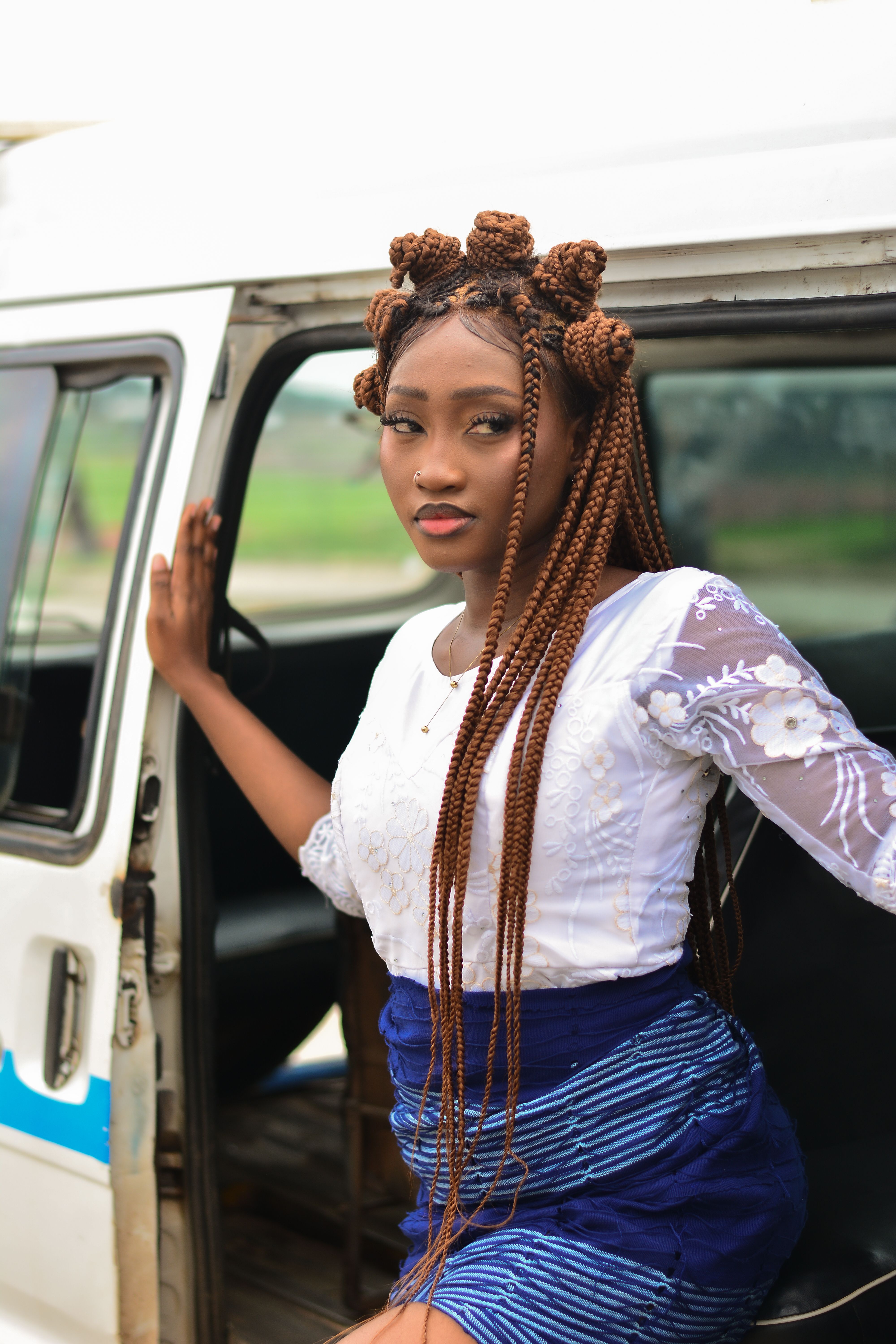 Confident young woman with stylish braids poses by a white van.