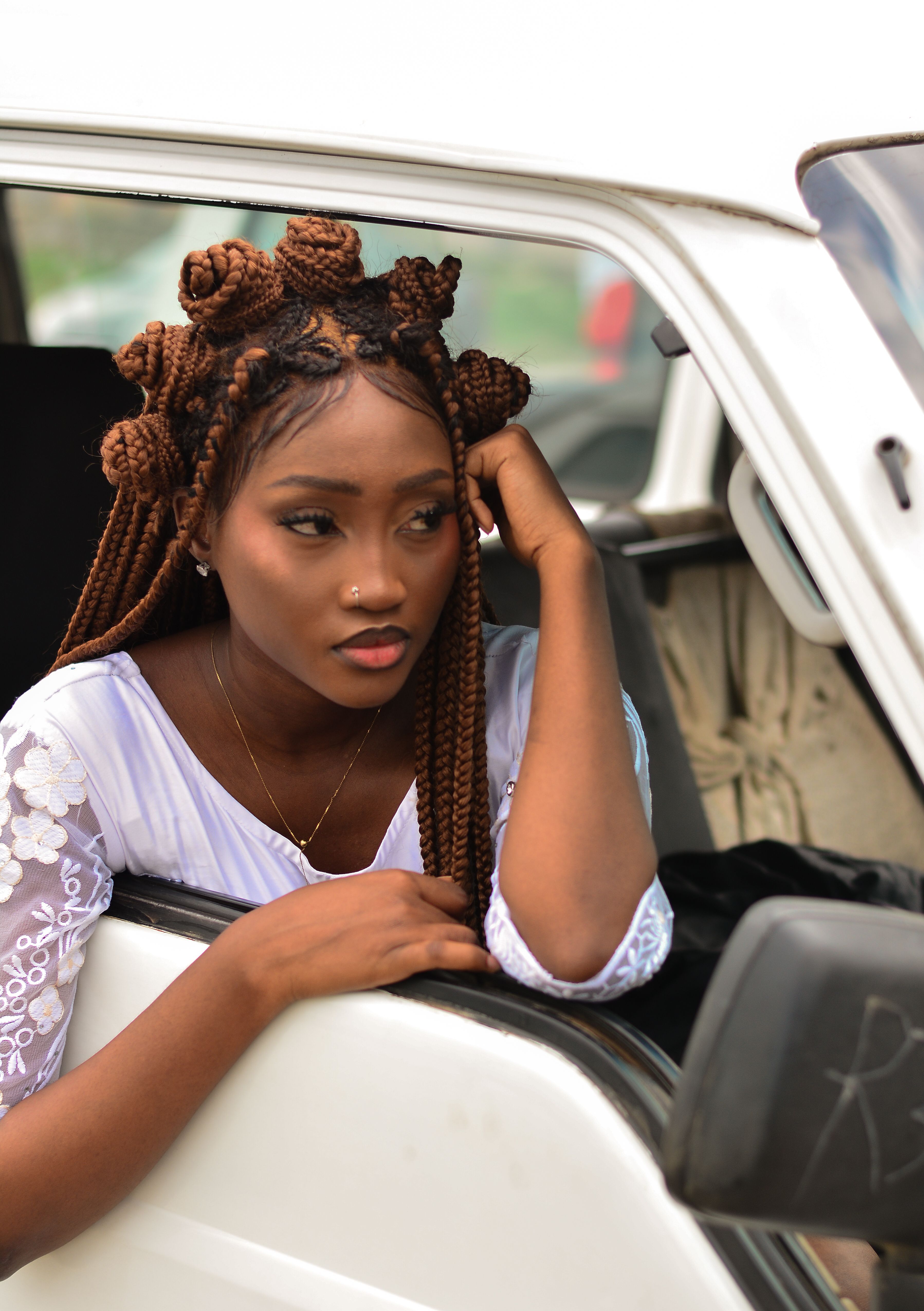 A woman with unique braided hairstyle leaning out of a car window, looking relaxed.