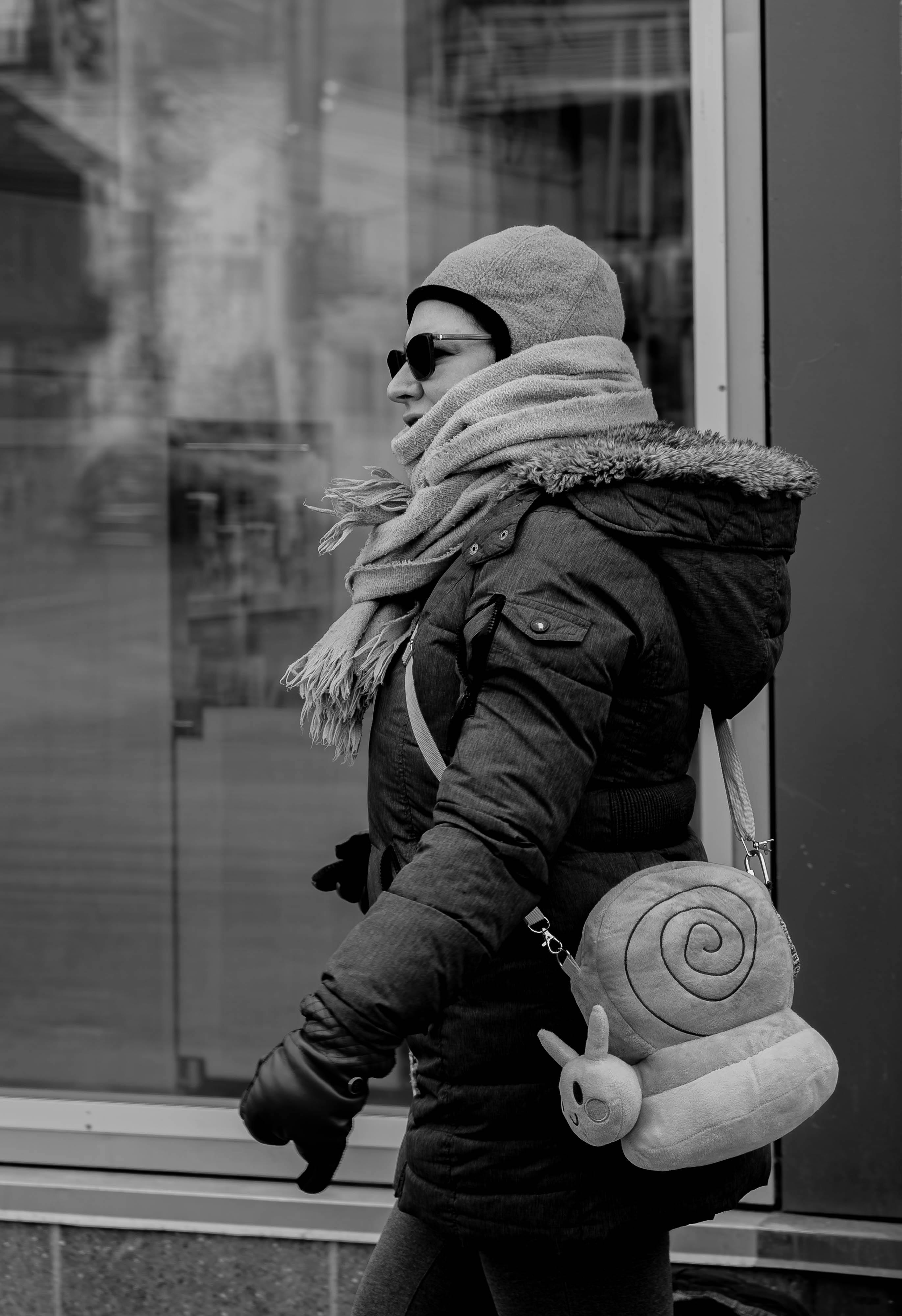 Gratis Donna in abiti invernali e zaino a forma di lumaca che cammina in città. Scatto in bianco e nero. Foto a disposizione