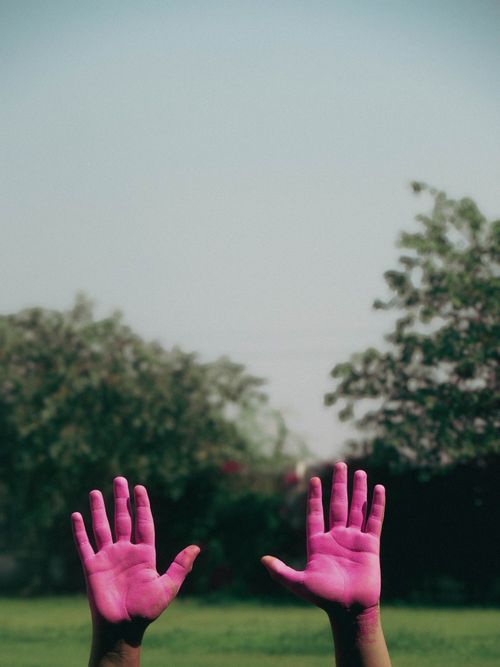 Free Two hands covered in pink powder paint raised against a lush outdoor backdrop. Stock Photo