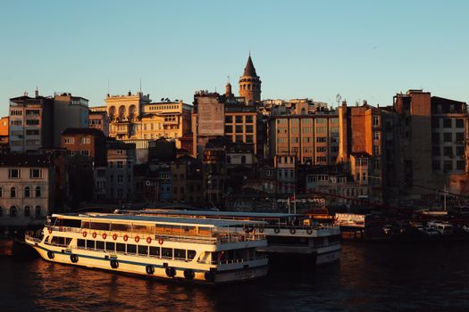Sunset over Istanbul with Galata Tower and ferryboats, showcasing urban architecture and maritime life.