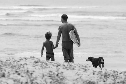 A father and child walk along the beach with their dog, enjoying a summer day.