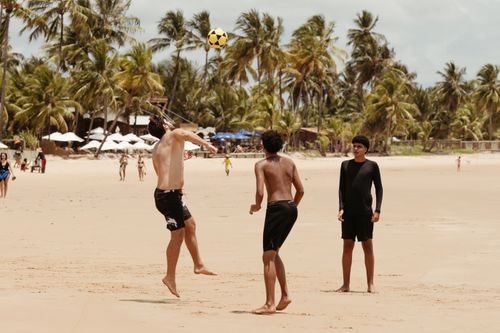 Free Group of teenagers playing beach soccer under palm trees on a sunny day. Stock Photo