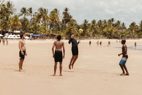 Free A group of men play soccer on a sandy beach surrounded by palm trees on a sunny day. Stock Photo