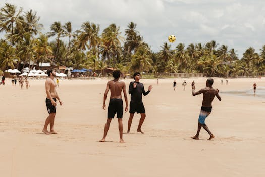 Friends enjoy a beach soccer game under palm trees, capturing the lively summer spirit.