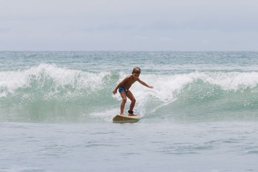 A young boy confidently surfing a gentle wave, showcasing skill and enjoyment in water sports.