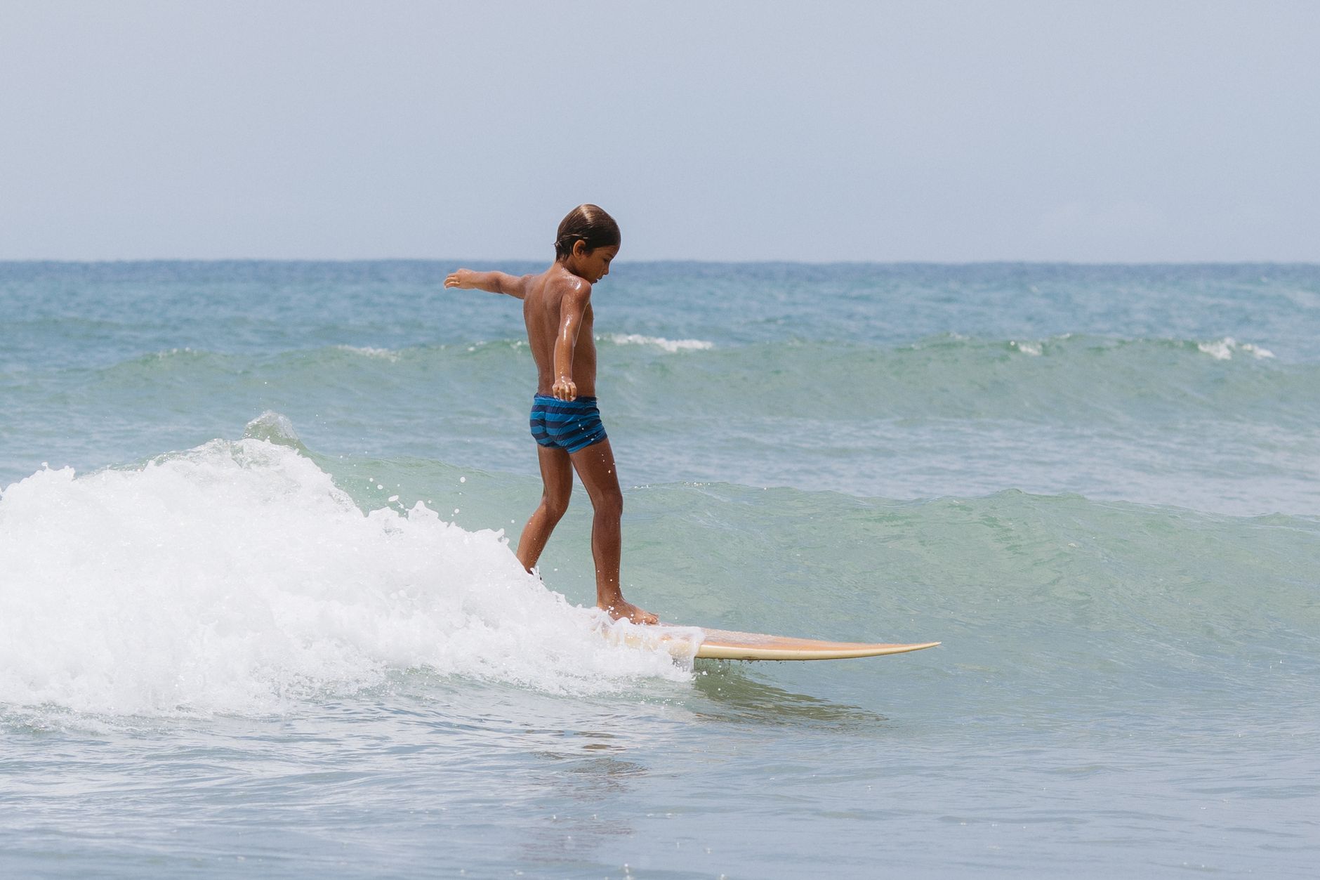 A young boy skillfully surfing on a gentle ocean wave during a sunny day at the beach.
