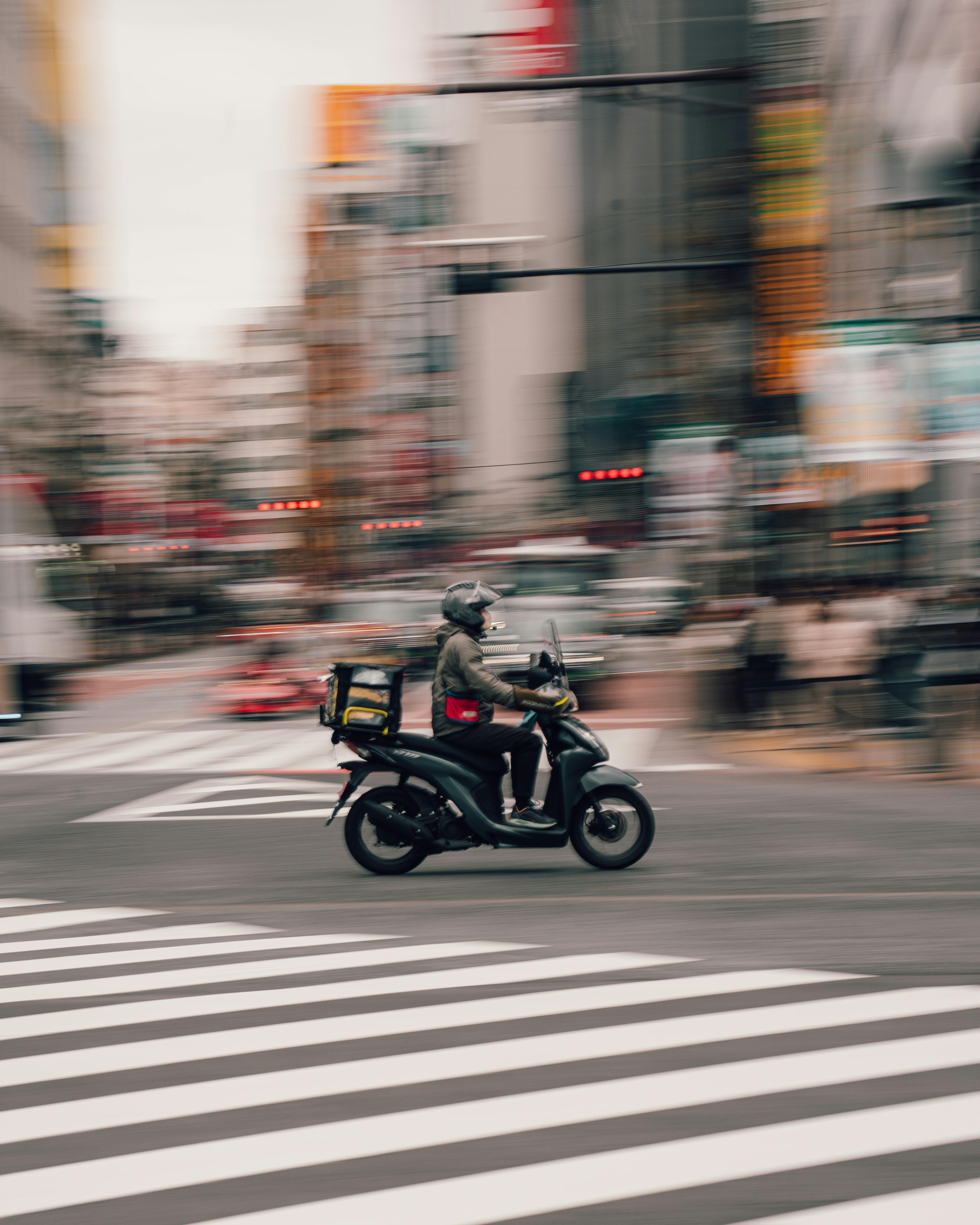 A delivery rider on a scooter speeds through a busy city street in Osaka, Japan, capturing urban hustle and motion.