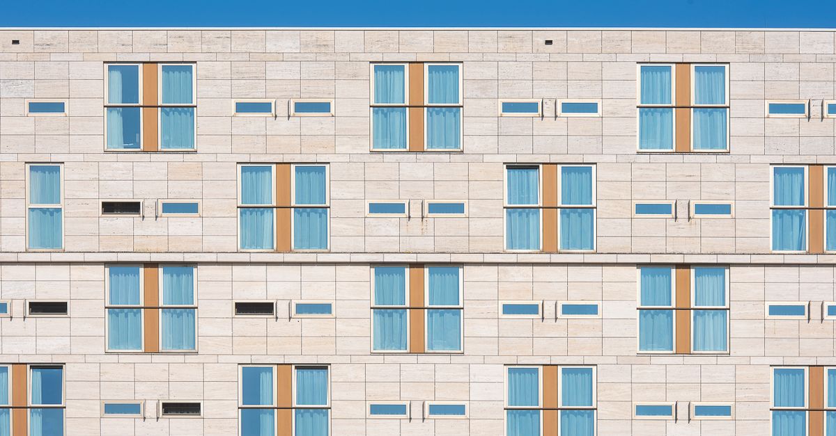 A minimalist view of a modern hotel facade with symmetrical windows and bright blue sky.