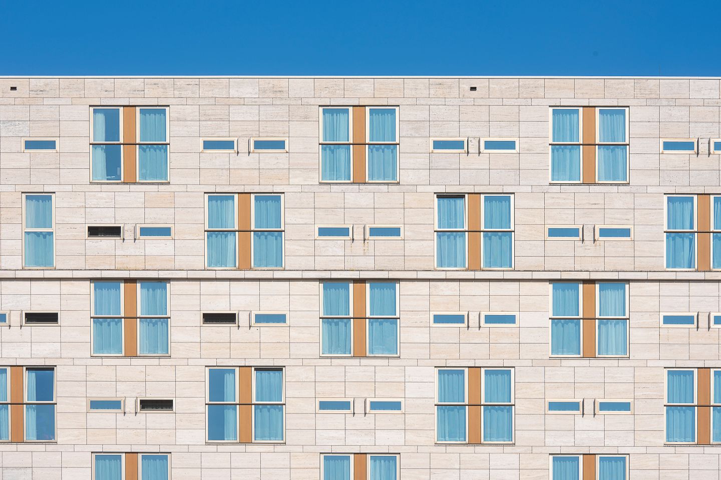 Rows of identical guest-room windows on a pale stone hotel facade under a clear blue sky