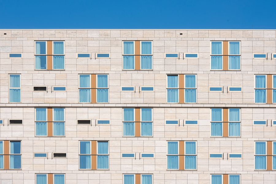 Rows of identical guest-room windows on a pale stone hotel facade under a clear blue sky