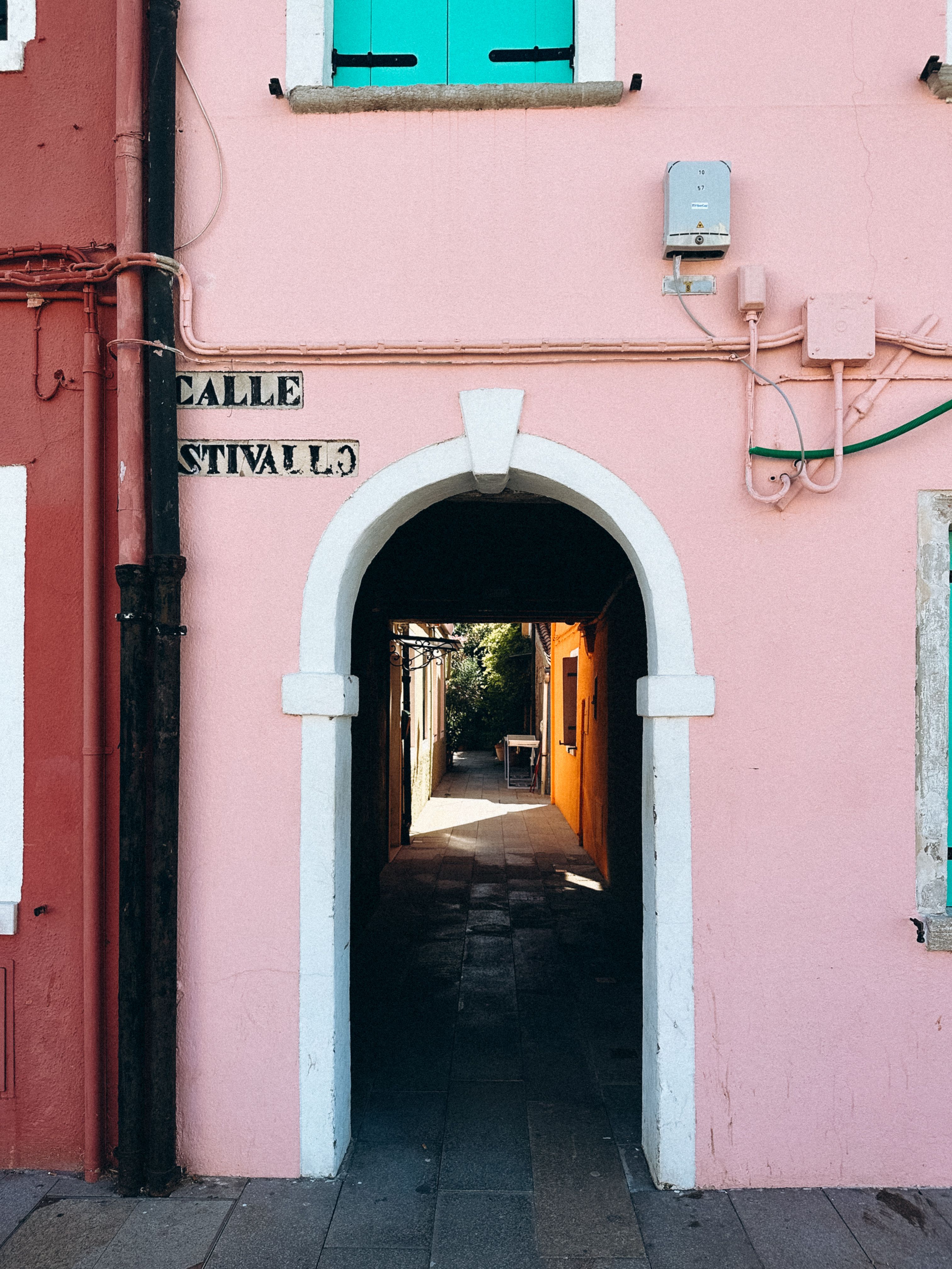 Colorful alleyway in Burano, Italy with vibrant walls and bright sunlight.
