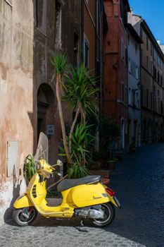 Yellow Vespa parked on a charming cobblestone street in Rome, Italy, highlighting Italian urban life.