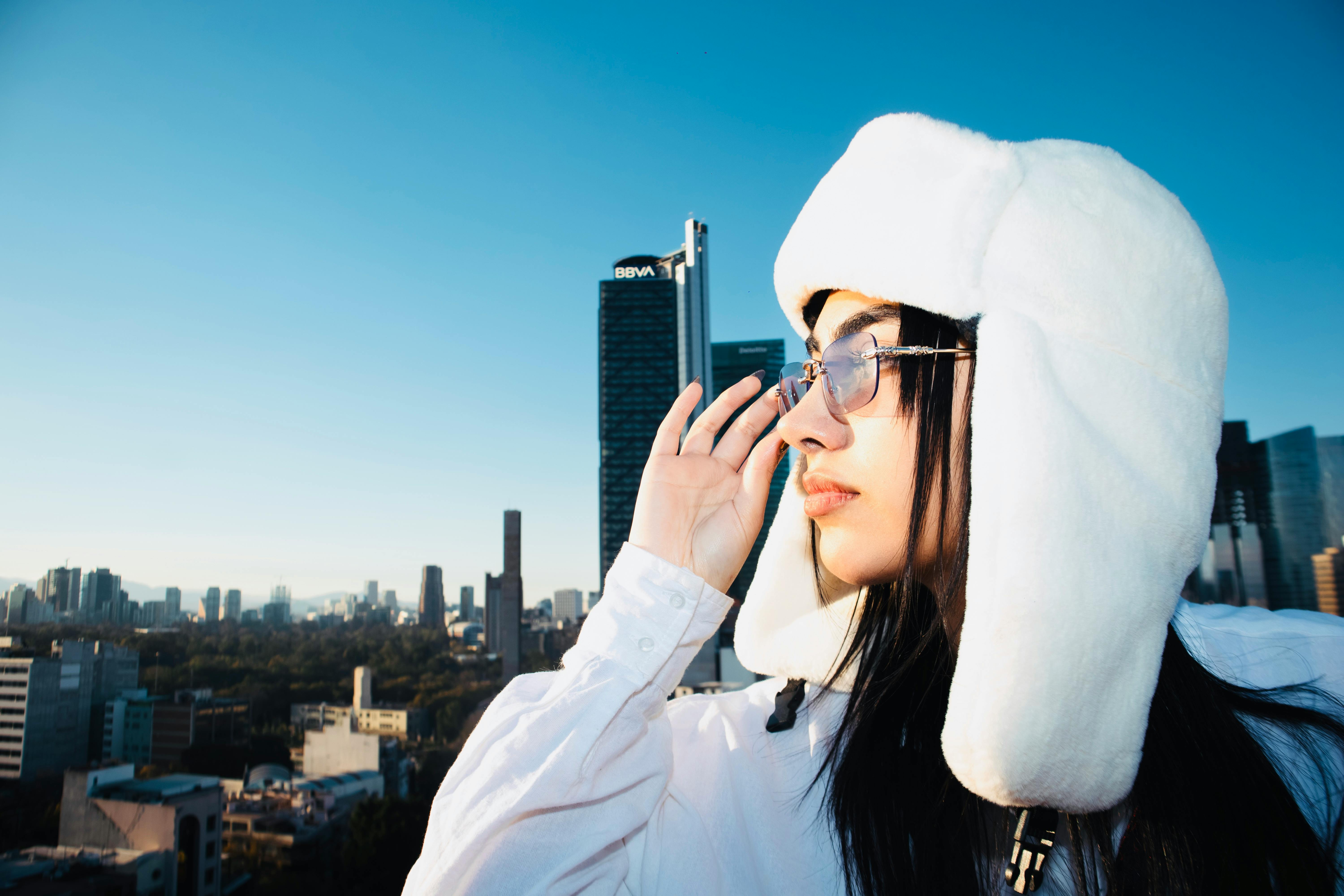 Woman wearing a white fur hat and sunglasses with Mexico City skyline in the background.