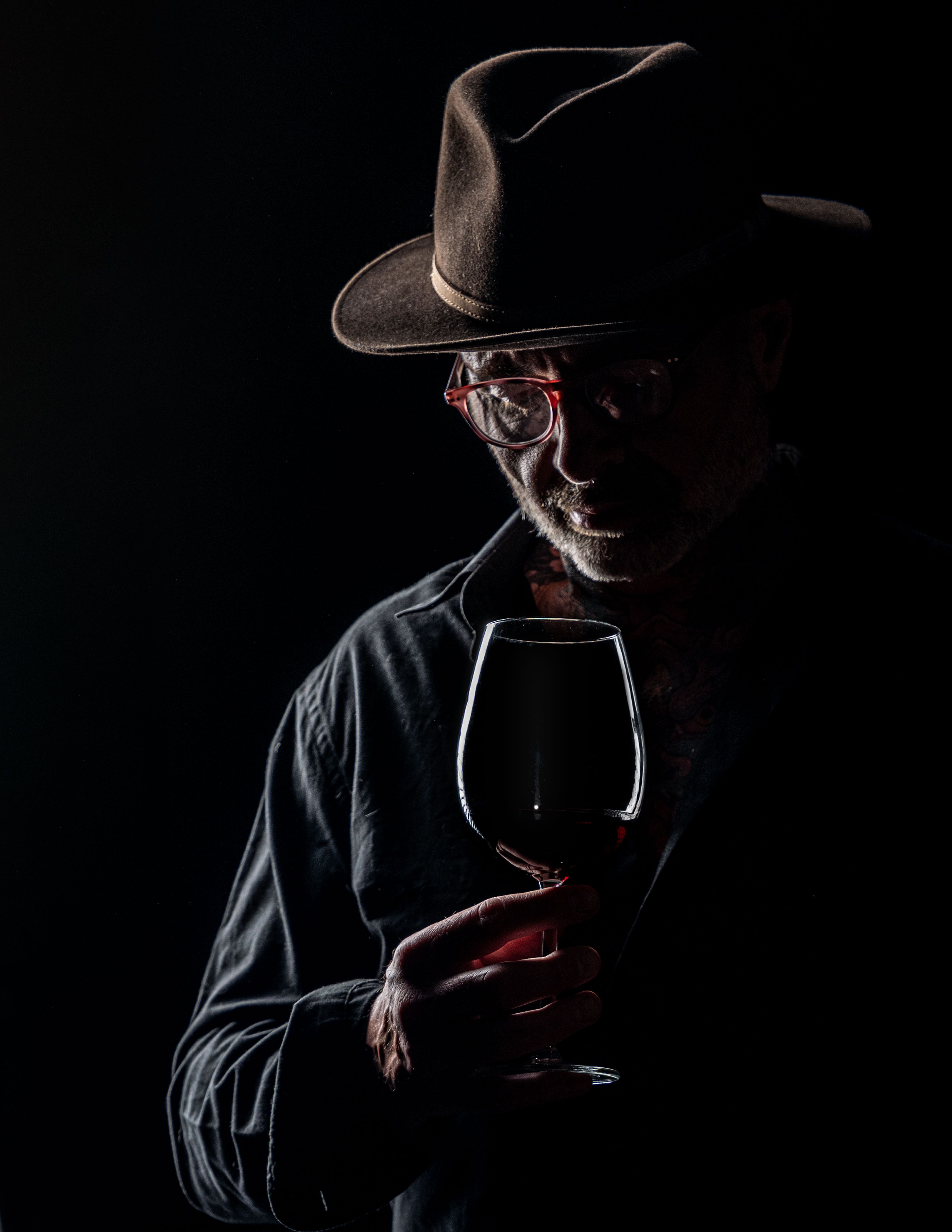 Dramatic low-key portrait of a man with a wine glass, highlighting textures and shadow interplay.