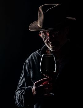 Dramatic low-key portrait of a man with a wine glass, highlighting textures and shadow interplay.