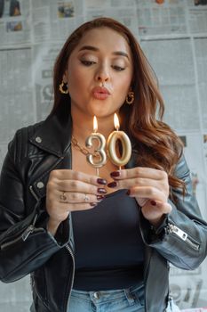 Adult woman in leather jacket holding birthday candles shaped as number 30.