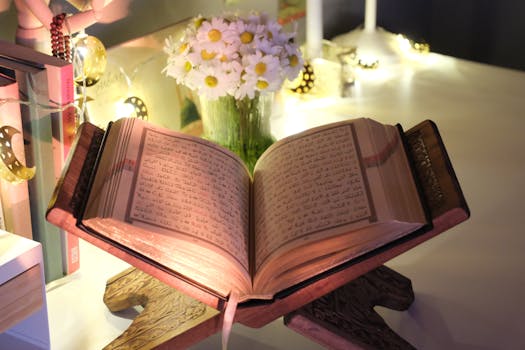 An open Quran illuminated by soft string lights on a wooden stand beside a bouquet of daisies.