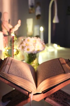 Open book on a wooden stand with candlelight ambiance, daisies in the background.