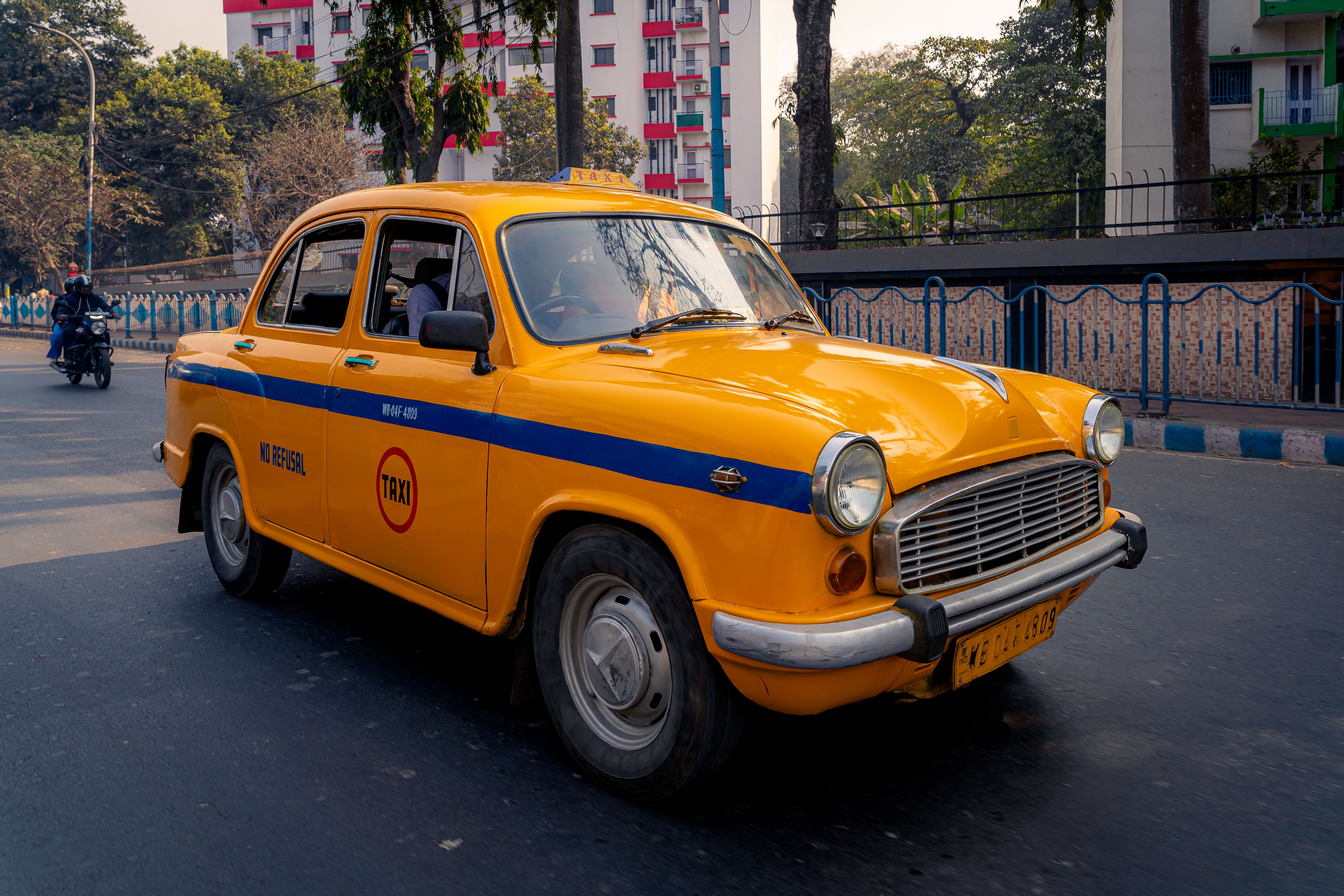 Iconic yellow taxi driving through the vibrant streets of Kolkata, India.