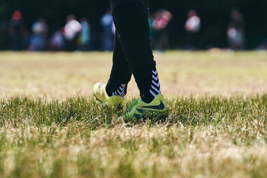 Soccer player wearing green cleats standing on grass field during daylight match.