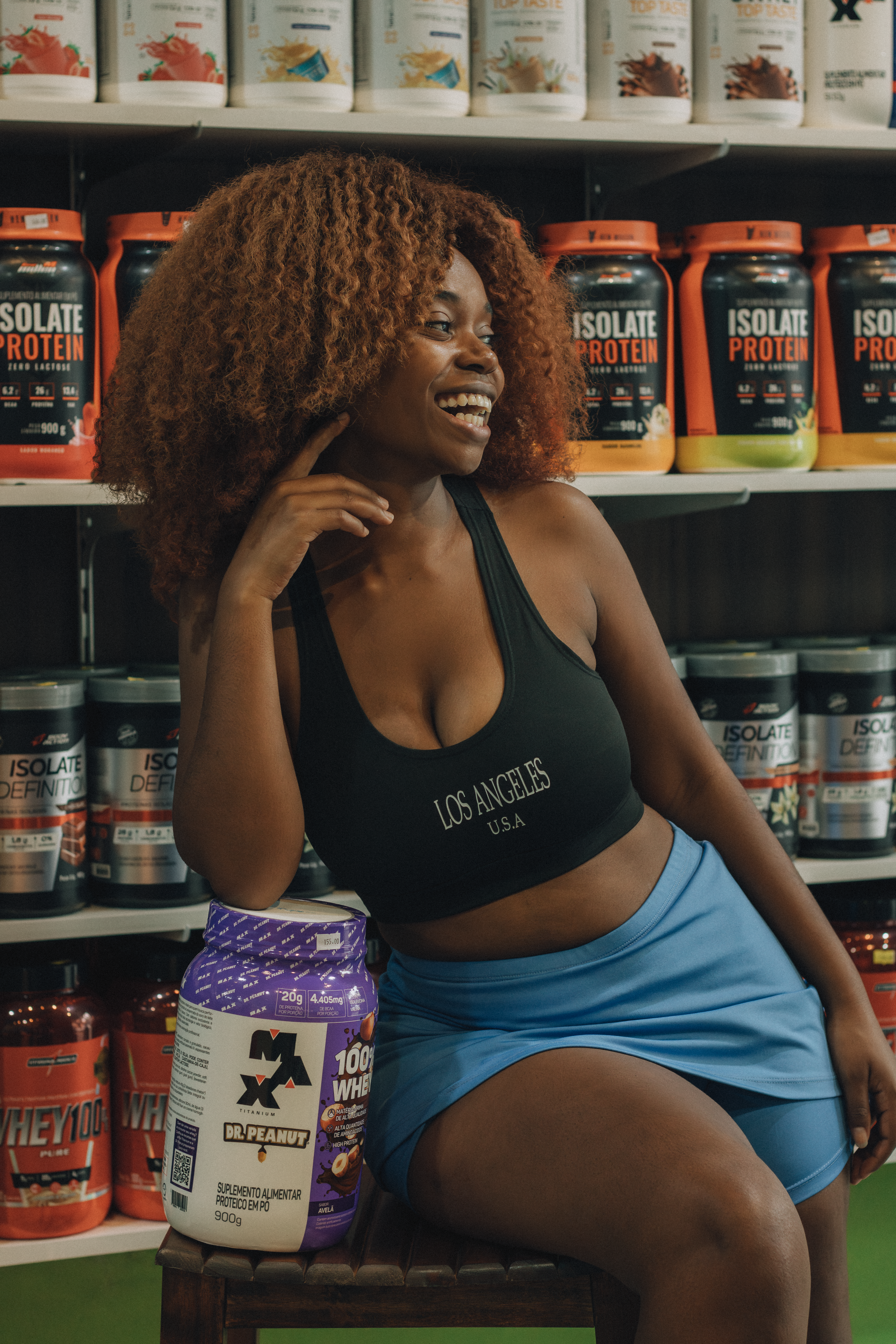 Happy woman in gym attire posing with whey protein and supplements on display.
