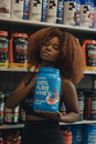 Young woman holding a 100% pure whey protein container in a supplement store.