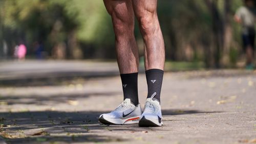 Free Close-up of male runner's legs wearing sneakers and black socks on a sunny park pathway. Stock Photo