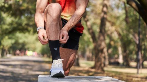 Free Close-up of a jogger adjusting socks before a run in a sunlit park, highlighting active lifestyle and fitness. Stock Photo