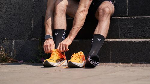 Free Athlete tying orange running shoes, preparing for a run outdoors in sunlight. Stock Photo