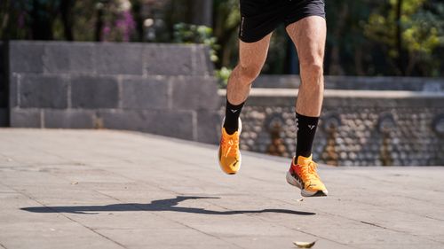 Free Male runner with orange shoes sprinting outdoors on a sunny day, showing athleticism. Stock Photo