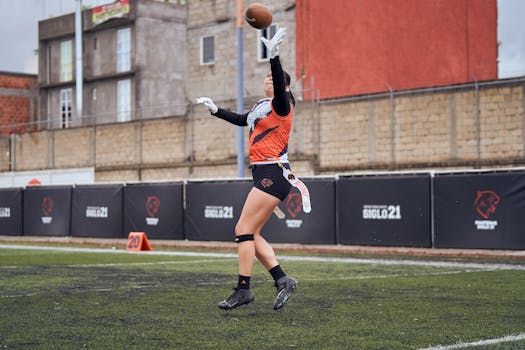 A female athlete jumps to catch a football during a game on an outdoor sports field.