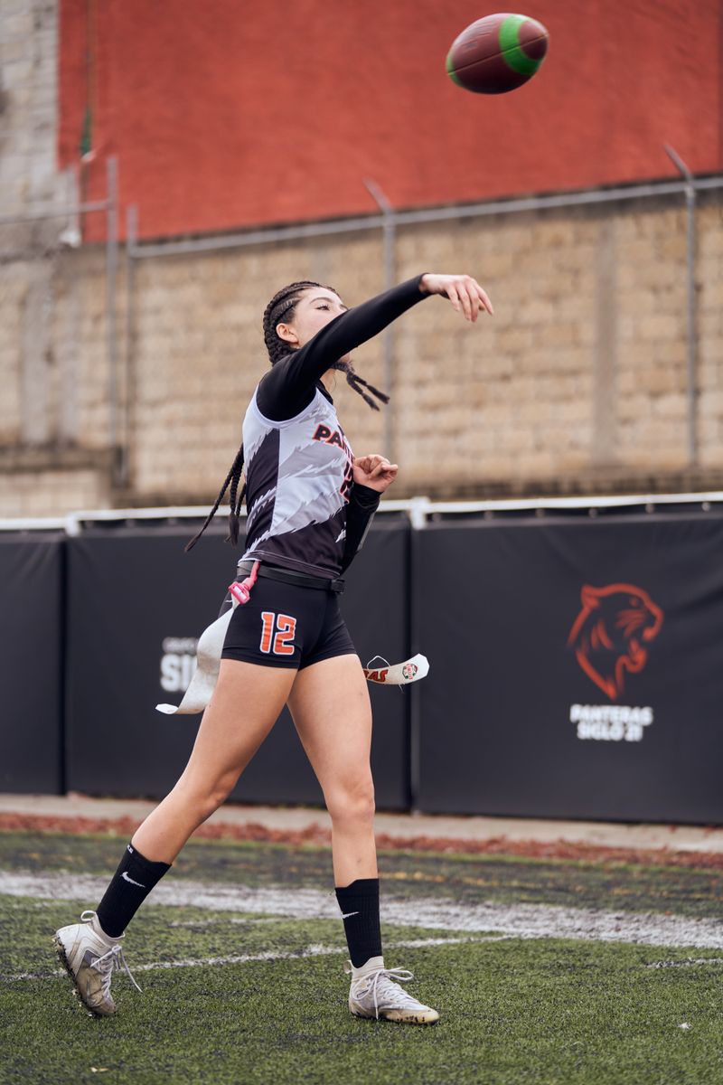 Young female athlete throwing a football on a sports field, showcasing athletic skills.