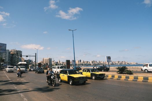 Vibrant street scene in Alexandria, Egypt, featuring yellow taxis and city skyline.
