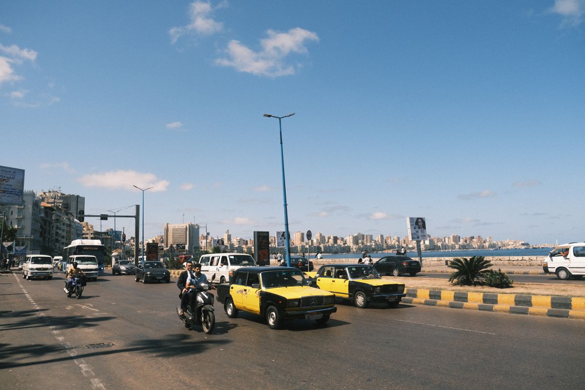 Vibrant street scene in Alexandria, Egypt, featuring yellow taxis and city skyline.