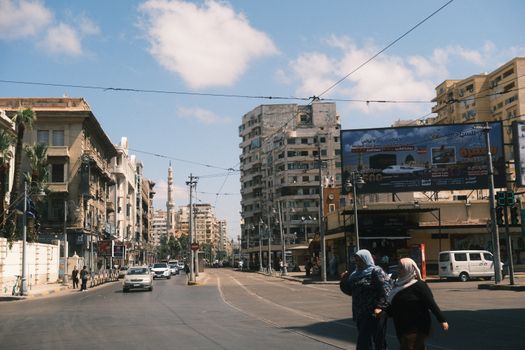 A lively street scene in Alexandria, showcasing historic and modern architecture under a clear sky.