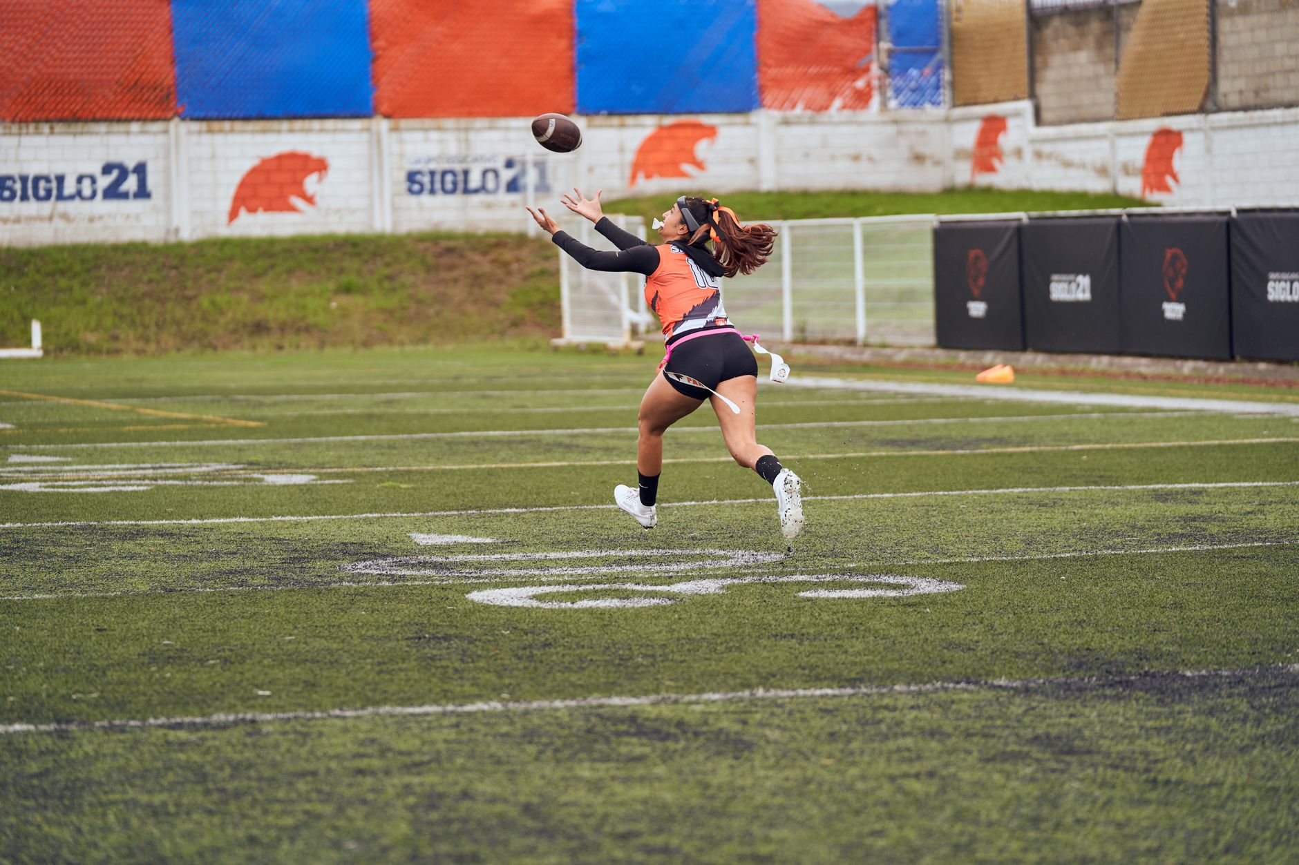 NCAA Football photo featuring Young female athlete in action catching a football on a sports field.